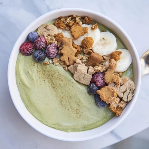 A creamy Gingerbread Cookie Matcha Breakfast Smoothie Bowl is topped with granola and candied ginger.