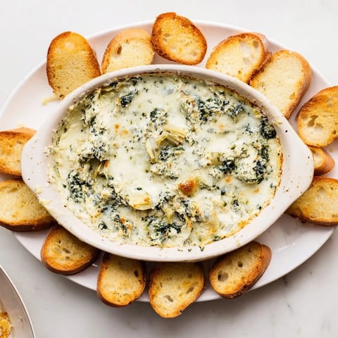 Creamy spinach artichoke dip, bubbling hot and served with golden toasted baguette slices.