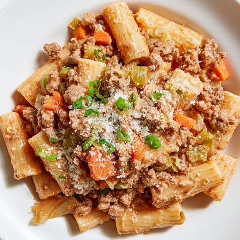 Steaming plate of Chaos Cooking Kimchi Ragu Pasta, with rich red sauce coating each pasta tube, ready to enjoy.