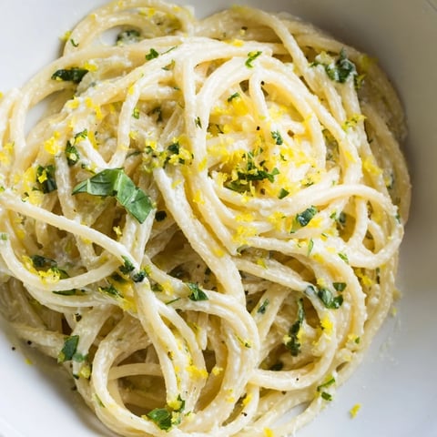 Freshly cooked spaghetti is coated in a creamy lemon ricotta pasta sauce, garnished with basil and extra Parmesan cheese for a vibrant Italian main dish.