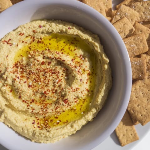 Golden brown rosemary crackers sit next to creamy hummus, the perfect holiday appetizer duo.