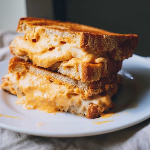 Sizzling close-up of a Spiked Grilled Cheese with oozing cheese and a vibrant, spicy sriracha glaze.
