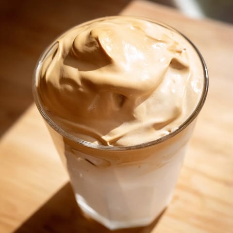 Golden-brown whipped Dalgona coffee layered over iced milk, showcasing thick foam and a sprinkle of cocoa for extra flair.  