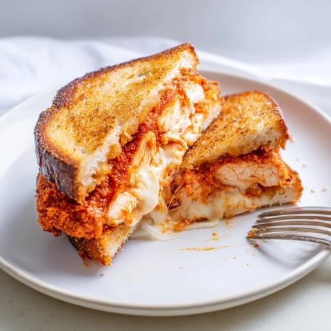 A close-up of Chicken Parm Grilled Cheese, featuring fried chicken cutlet, fresh basil, and garlicky toasted bread.