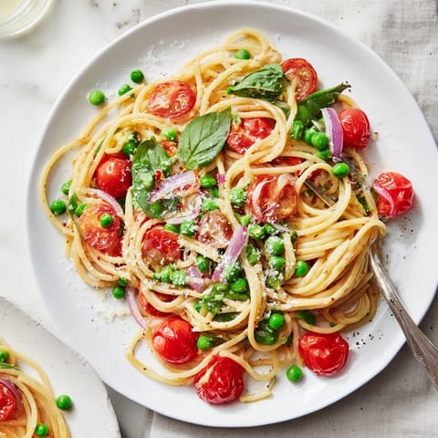 A vibrant bowl of Spring Veggie One-Pot Spaghetti garnished with fresh basil and grated Parmesan cheese.
