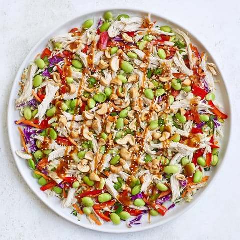Edamame Crunch Chicken Salad plated in a white bowl, featuring shredded chicken, crisp vegetables, and a drizzle of Asian-inspired ginger dressing for a light lunch.  