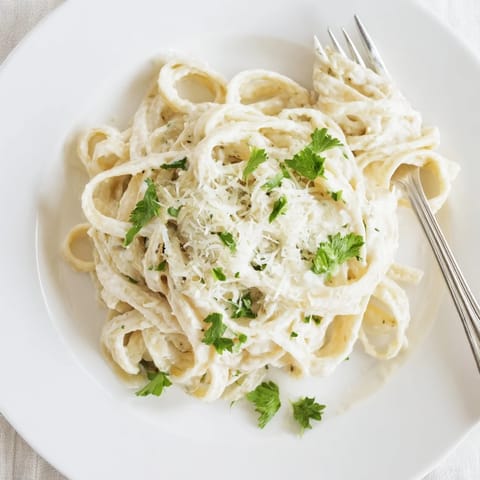 A close-up of velvety cauliflower Alfredo pasta twirled on a fork, topped with extra Parmesan and parsley.  
