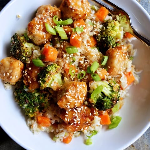 A close-up of One Pan Honey Garlic Chicken Broccoli Rice garnished with sesame seeds and green onions.