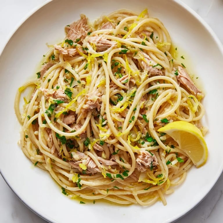 This photo features the finished Lemon-Garlic Tuna Spaghetti, garnished with fresh parsley and lemon wedges.