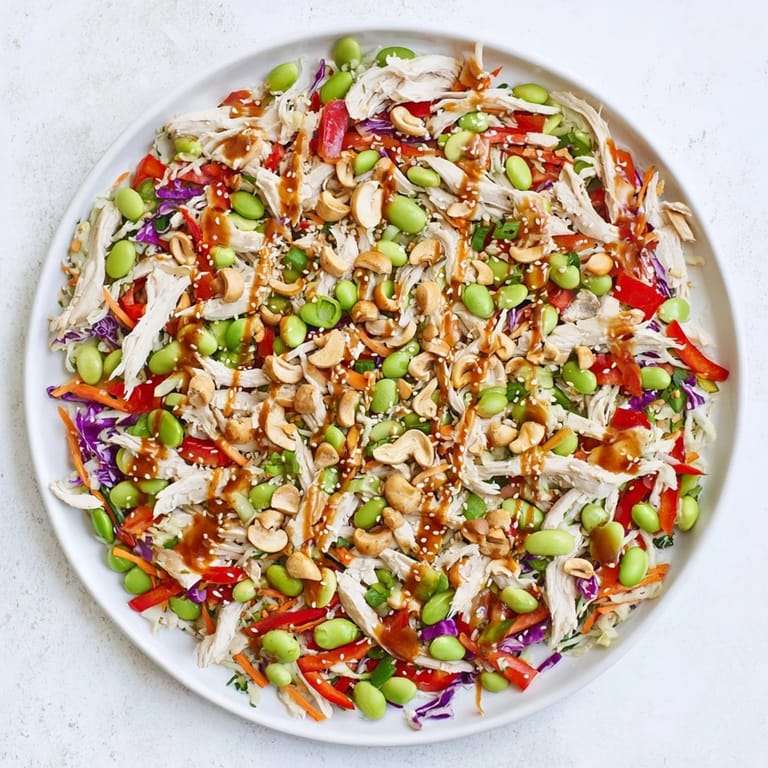 Edamame Crunch Chicken Salad plated in a white bowl, featuring shredded chicken, crisp vegetables, and a drizzle of Asian-inspired ginger dressing for a light lunch.  