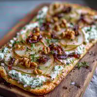 Golden Goat Cheese & Pear Flatbread with hot honey drizzle, topped with caramelized onions and crunchy walnuts on a serving board.